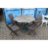 A hardwood folding garden table with four chairs and a parasol stand.