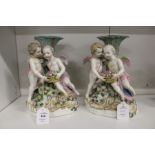 A pair of 19th century porcelain figural candlesticks, each with a pair of cherubs holding a