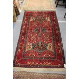 A Persian rug, red ground with stylized bird and tree motifs.