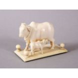 A 19TH CENTURY INDIAN CARVED IVORY FIGURE OF A NANDI COW AND CALF on stand, 7cm long.