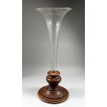 A LARGE FACETED GLASS TRUMPET-SHAPED VASE set into a circular wooden base, 2 ft. 9 in. high.