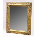 A LARGE GILT BEVELLED MIRROR with scrolling decoration, 5 ft. 3 in. high, 4 ft. 2 in. wide.