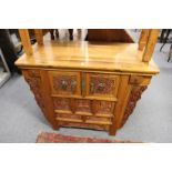 A Chinese altar cabinet with carved decoration and various drawers and cupboard doors.