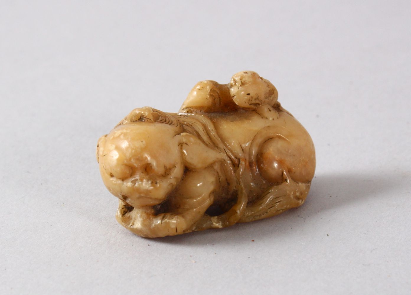 A CHINESE SOAPSTONE FIGURE OF A LION DOGs, the small carving depicts a recumbent lion dog with a