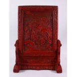 A CHINESE RELIEF CINNABAR LACQUER STYLE TABLE SCREEN & STAND, with scenes of immortal figures in