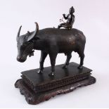 AN IDIAN JAIPUR SCHOOL BRONZE MODEL OF A COW, with a boy seated upon its back, mounted to a carved