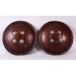 A GOOD PAIR OF INDIAN PAINTED AND LACQUERED LEATHER SHEILDS, each with four glass roundels,