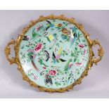A CHINESE CELEDON CIRCULAR DISH, painted with birds and flowers in an ormolu frame with handles,