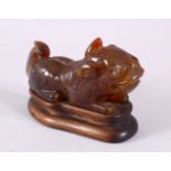 A CHINESE CARVED AGATE FIGURE OF A RECLINING BEAST, 13cm long, on a wooden stand.