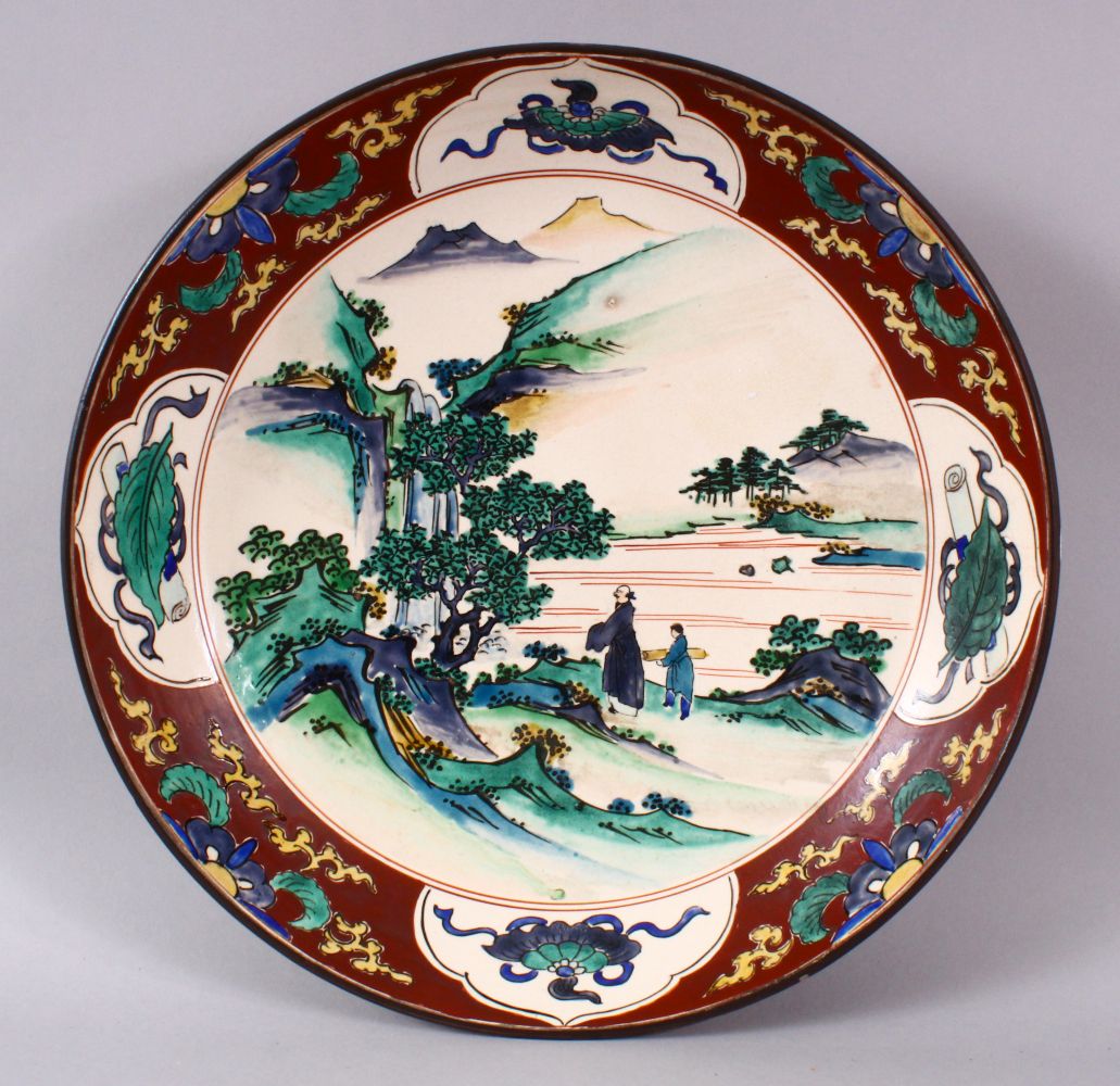 A JAPANESE MEIJI PERIOD KUTANI CHARGER, decorated with scenes of figures in native landscapes, the