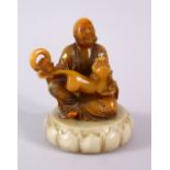 A CHINESE CARVED AMBER COLOUR SOAPSTONE FIGURE OF LOUHAN - in a seated pose with a kyllin and a