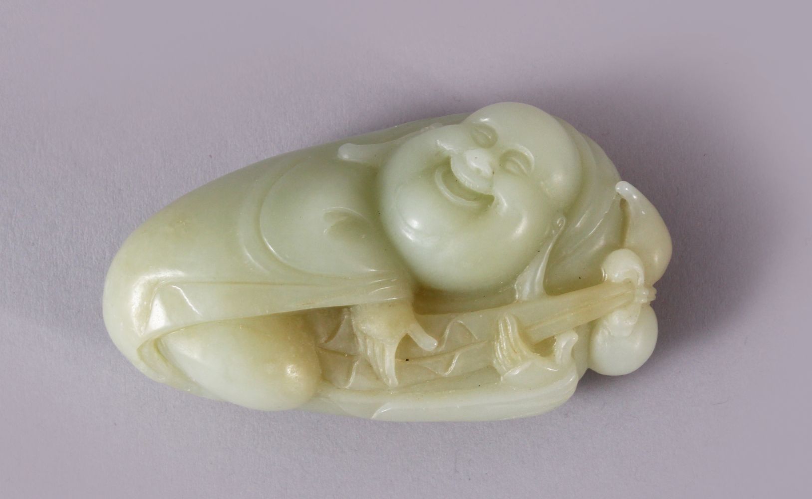 A CHINESE CARVED JADE FIGURE / PENDANT OF BUDDHA, in a recumbent position holding a tied double