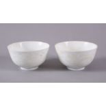 A PAIR OF CHINESE WHITE MONOCHROME GLAZED PORCELAIN TEA BOWLS - the body decorated with scenes of