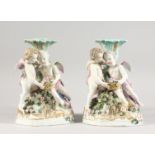 A PAIR OF 19TH CENTURY MEISSEN STYLE PORCELAIN CANDLESTICK GROUPS of cupids holding baskets Cross