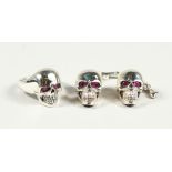A PAIR OF SILVER SKULL CUFF LINKS AND RING, with ruby eyes.