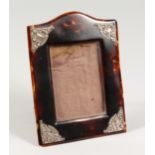 A SILVER MOUNTED UPRIGHT TORTOISESHELL PHOTOGRAPH FRAME with serpentine top and leather back, 6