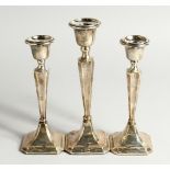 A SET OF THREE SILVER CANDLESTICKS with loaded bases. Chester 1904 & 1924 8ins and 6ins high