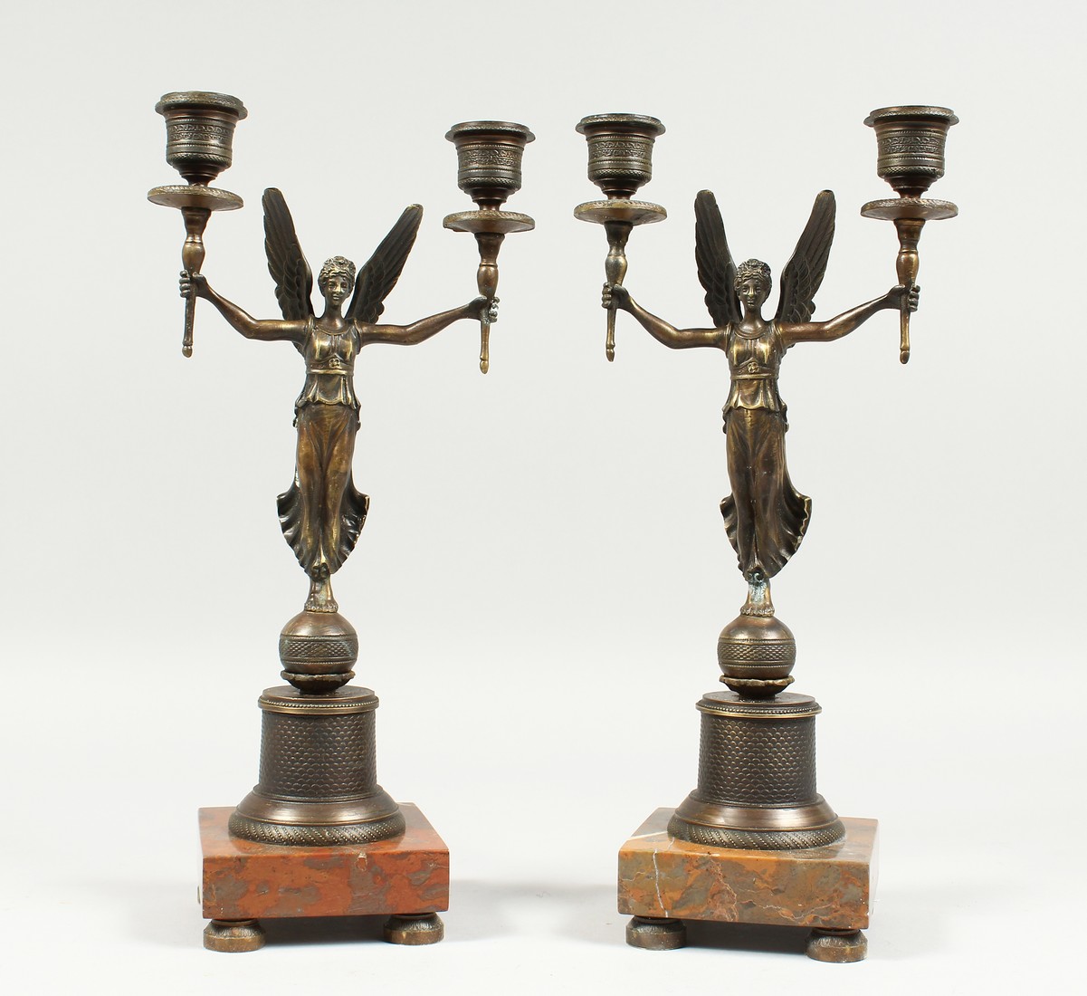 A PAIR OF EMPIRE BRONZE WINGED LADIES TWO LIGHT CANDLESTICKS on a square base. 13ins high