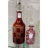 A ruby tinted cut glass decanter and stopper together with a floral decorated cranberry glass