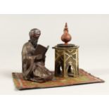 A PAINTED BRONZE OF AN ARAB, reading on a carpet. 5.5ins long.