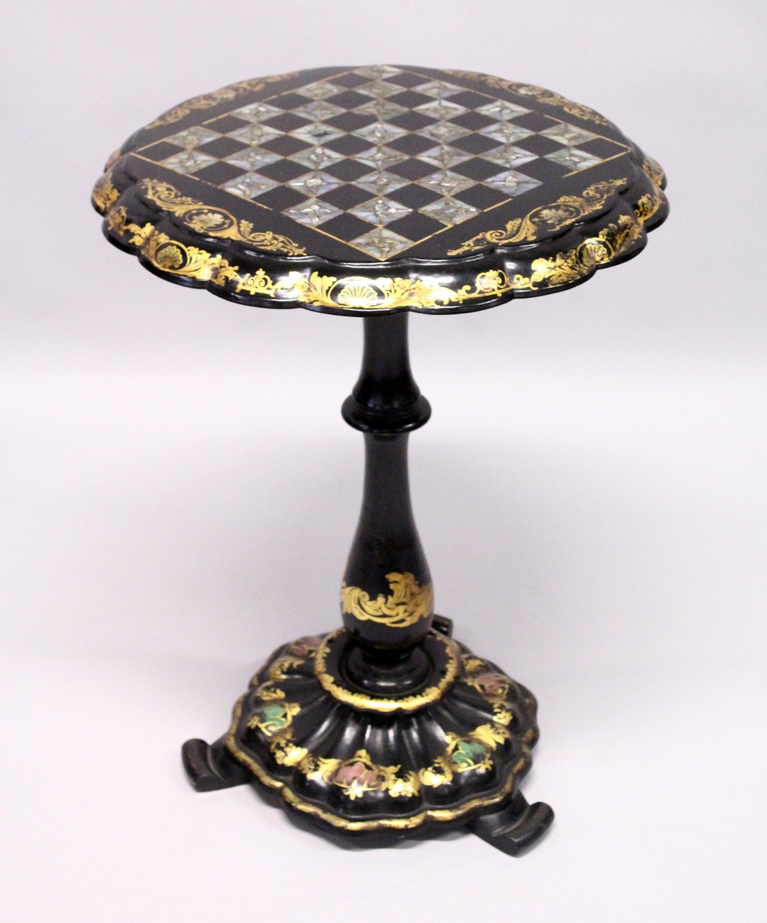 A VICTORIAN BLACK AND GILT PAPIER MACHE TILT TOP GAMES TABLE, with inlaid chess board in mother of