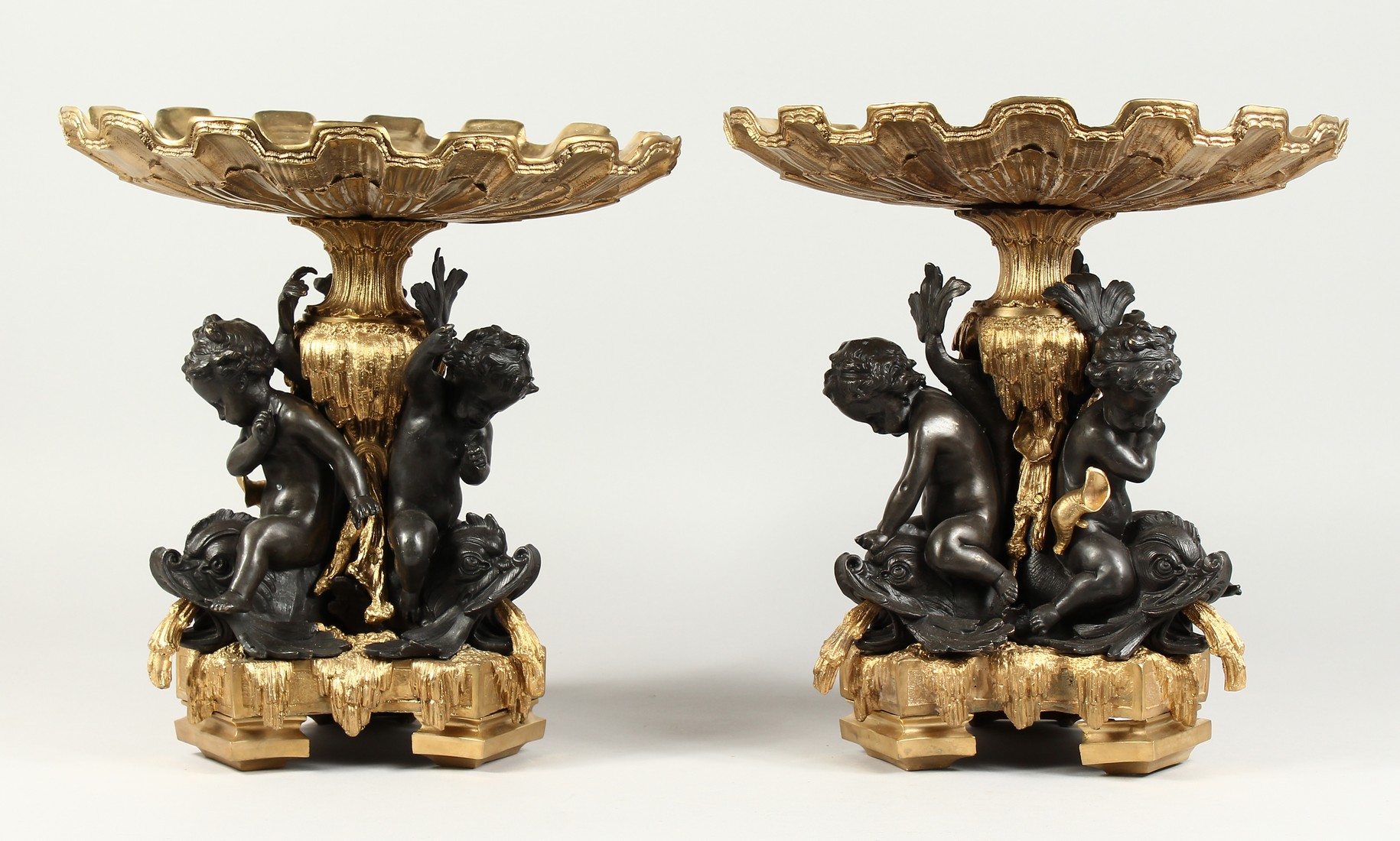 A GOOD PAIR OF BRONZE AND GILT BRONZE COMPORTS with shell shaped tops, three cupid supports. 13ins