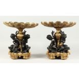 A GOOD PAIR OF BRONZE AND GILT BRONZE COMPORTS with shell shaped tops, three cupid supports. 13ins