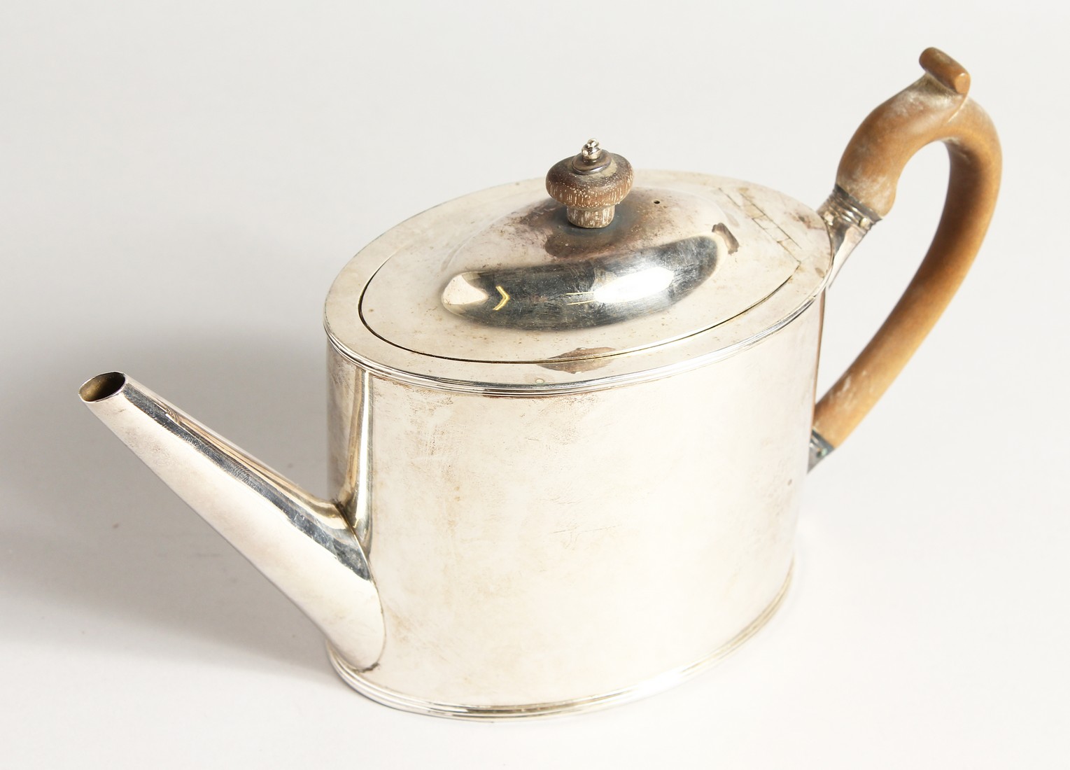 A GEORGE III PLAIN SILVER OVAL TEA POT and cover with wooden handles. London 1789, maker I. O.