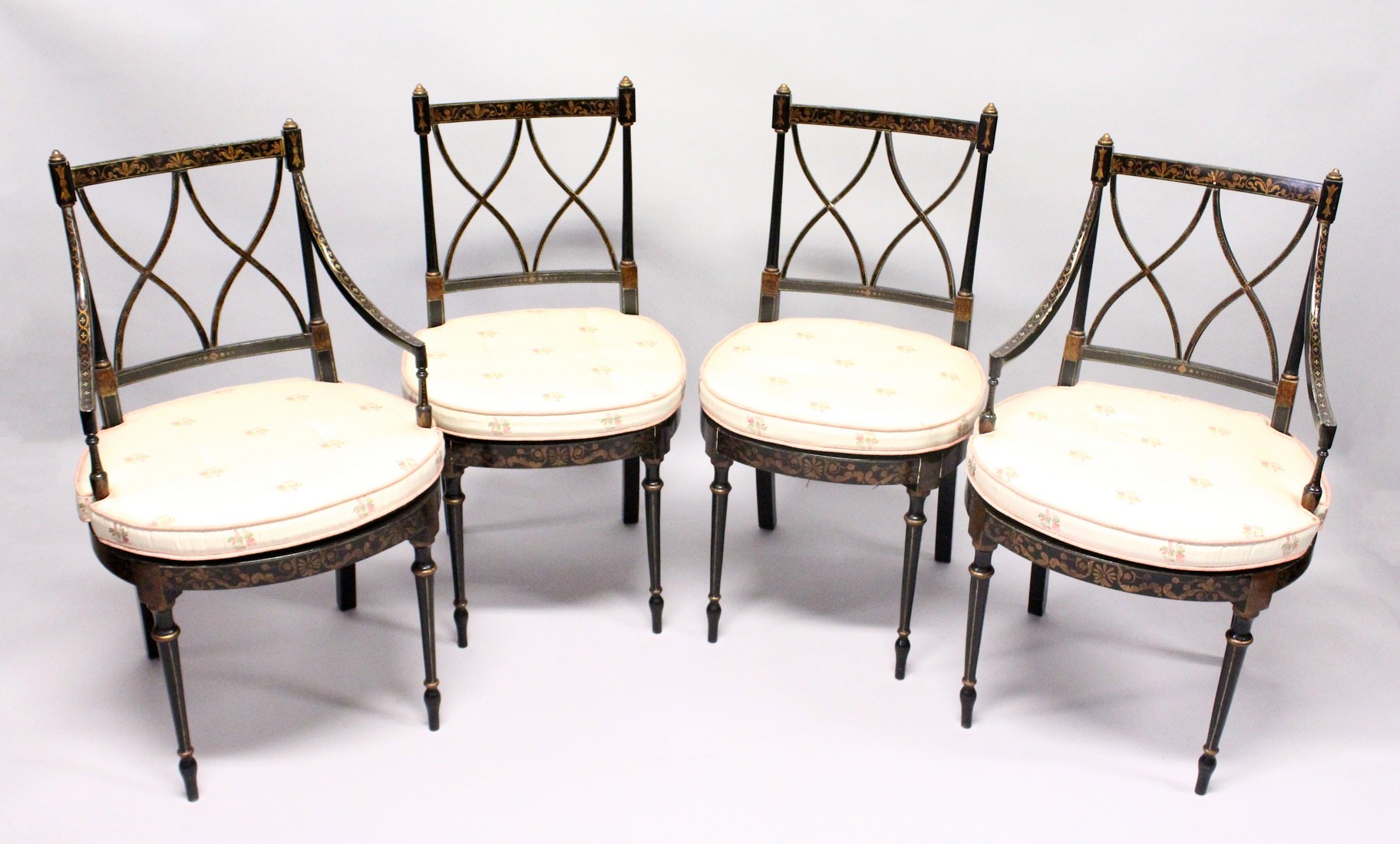 A SET OF FOUR BLACK AND GILT CHAIRS, two with arms, with cross fret backs and cane seats.