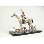 A SILVERED BRONZE GROUP HORSE AND RIDER, with their dogs, on a wooden base. 17ins long, 12ins high.