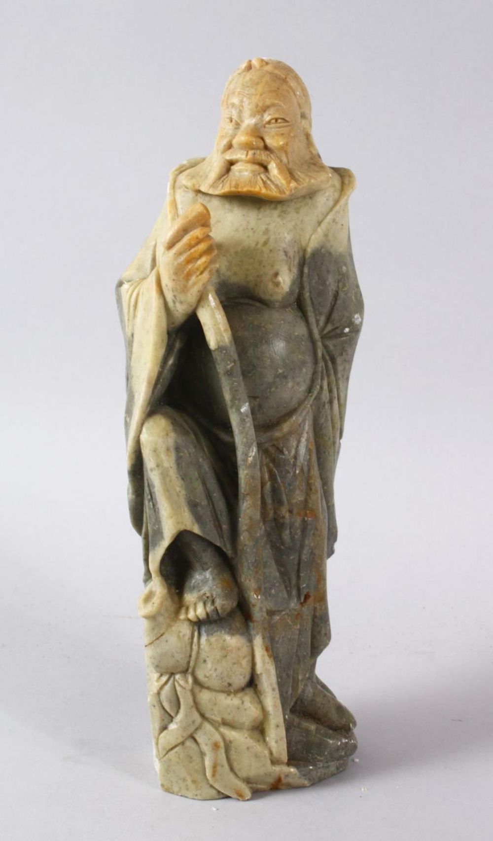 A LARGE CHINESE SOAPSTONE CARVING OF AN IMMORTAL, stood upon a rocky outcrop with a double groud,