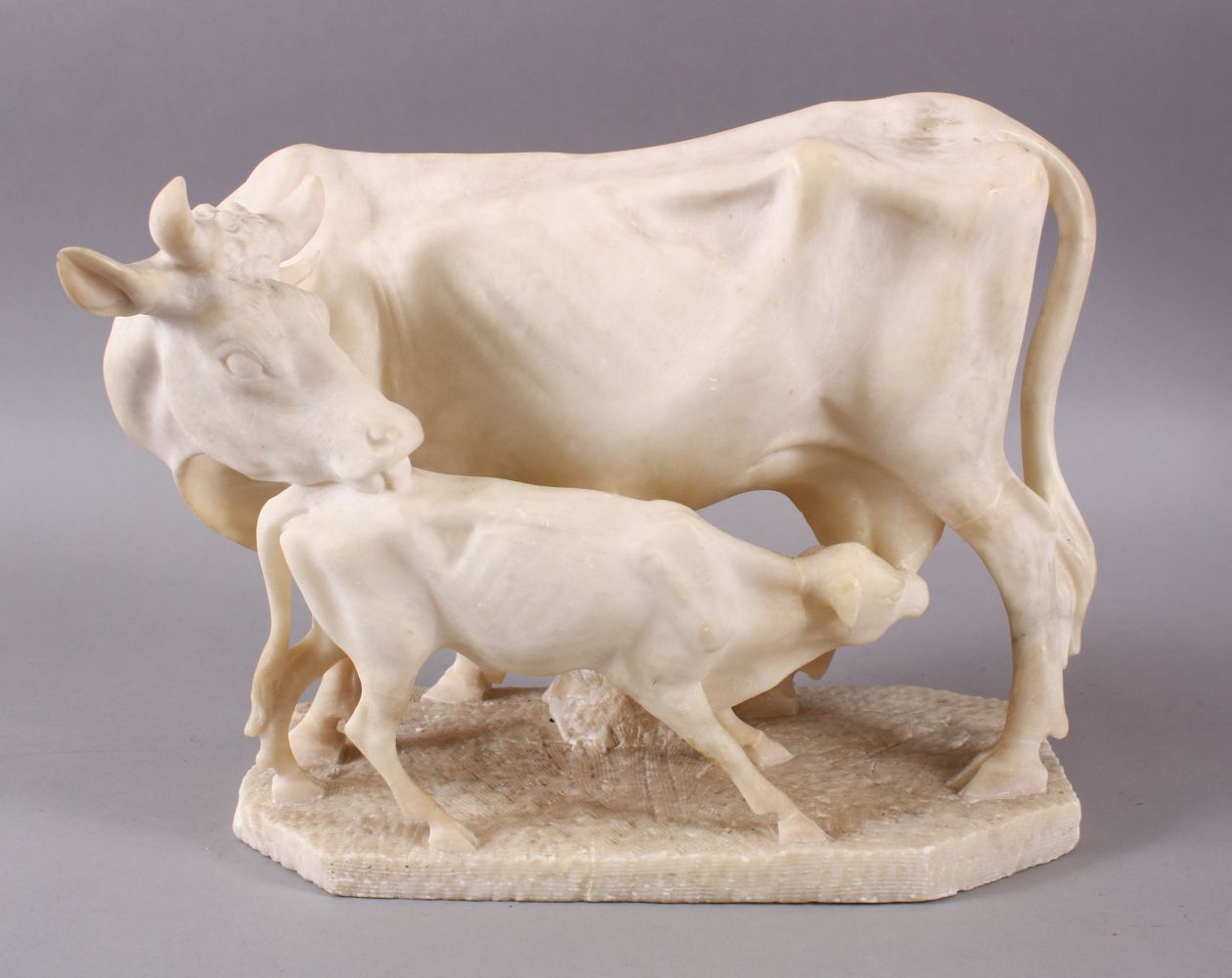 A 19TH CENTURY INDIAN ALABASTER MODEL OF NANDI COWS - the larger cow depicted with young, 25cm