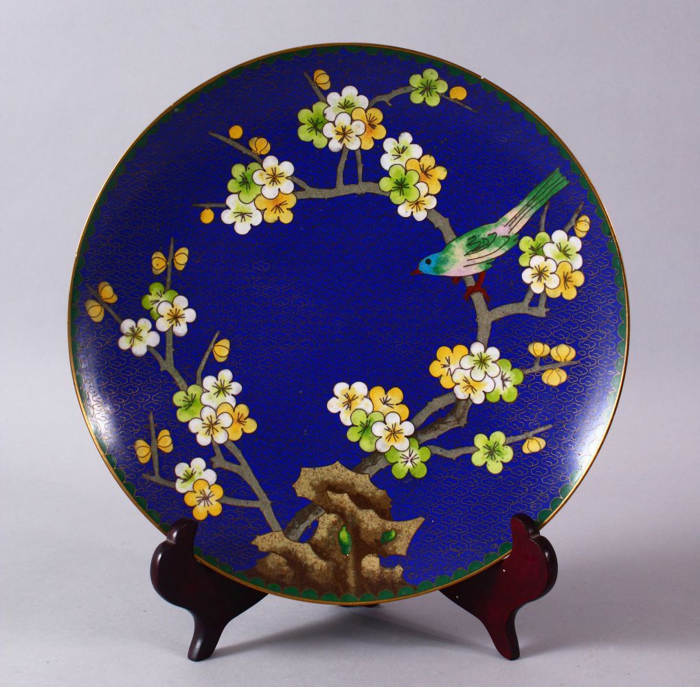 A CHINESE CLOISONNE PLATE & STAND - the dish with a royal blue ground with prunus decoration, 23cm.