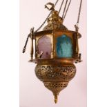 A GOOD BRASS QAJAR HANGING LAMP, with coloured glass panels, bird finial, the actual lamp