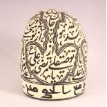 AN ISLAMIC FABRIC CALLIGRAPHIC HEAD PIECE / HAT - with a beige ground and black calligraphy and