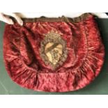 AN INTERESTING CRIMSON VELVET HANDBAG, applied with an earlier gold thread embroidery armorial badge