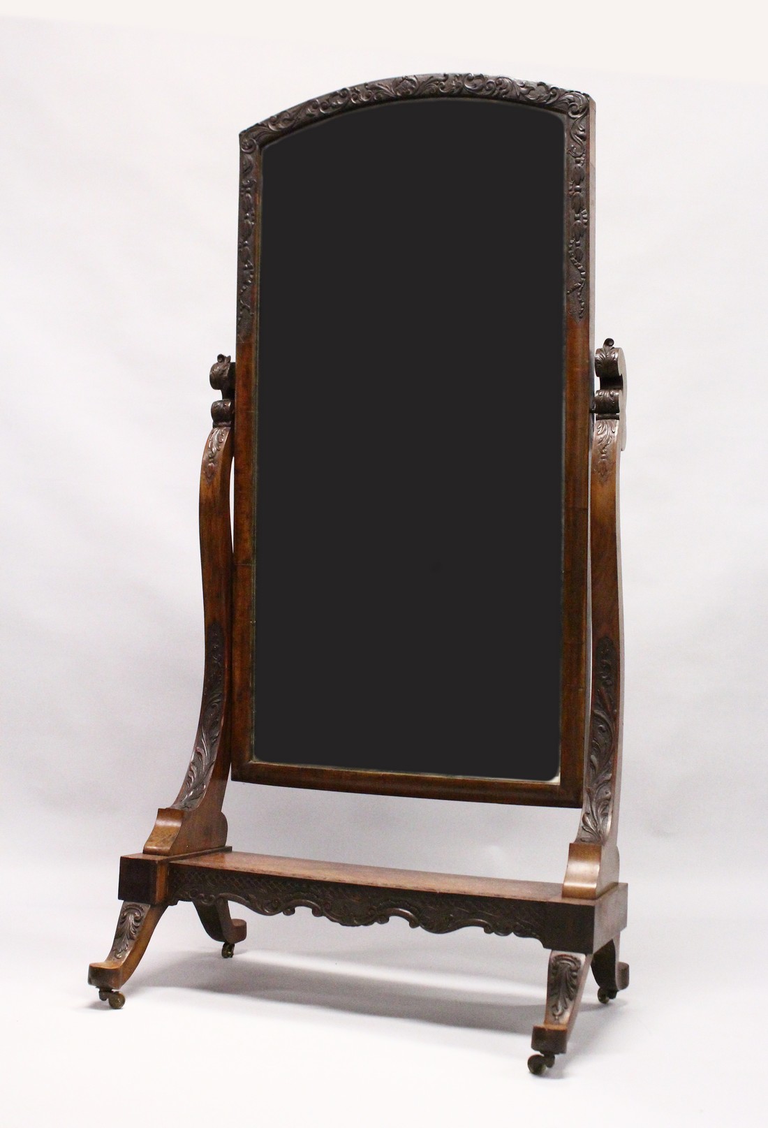 A GOOD IRISH CARVED MAHOGANY CHEVAL MIRROR, mirrored plate, the stand ending on castors. 4ft x 2ft