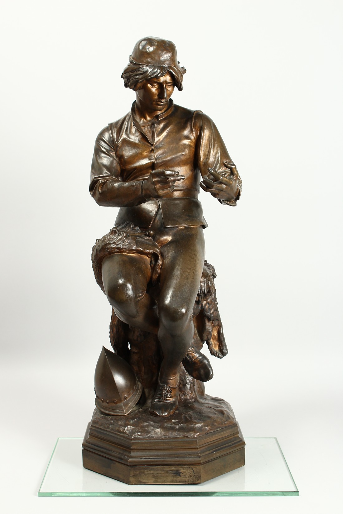C. MANICLIER. A LARGE BRONZE OF A YOUNG MAN, seated on a tree stump with octagonal base. Signed