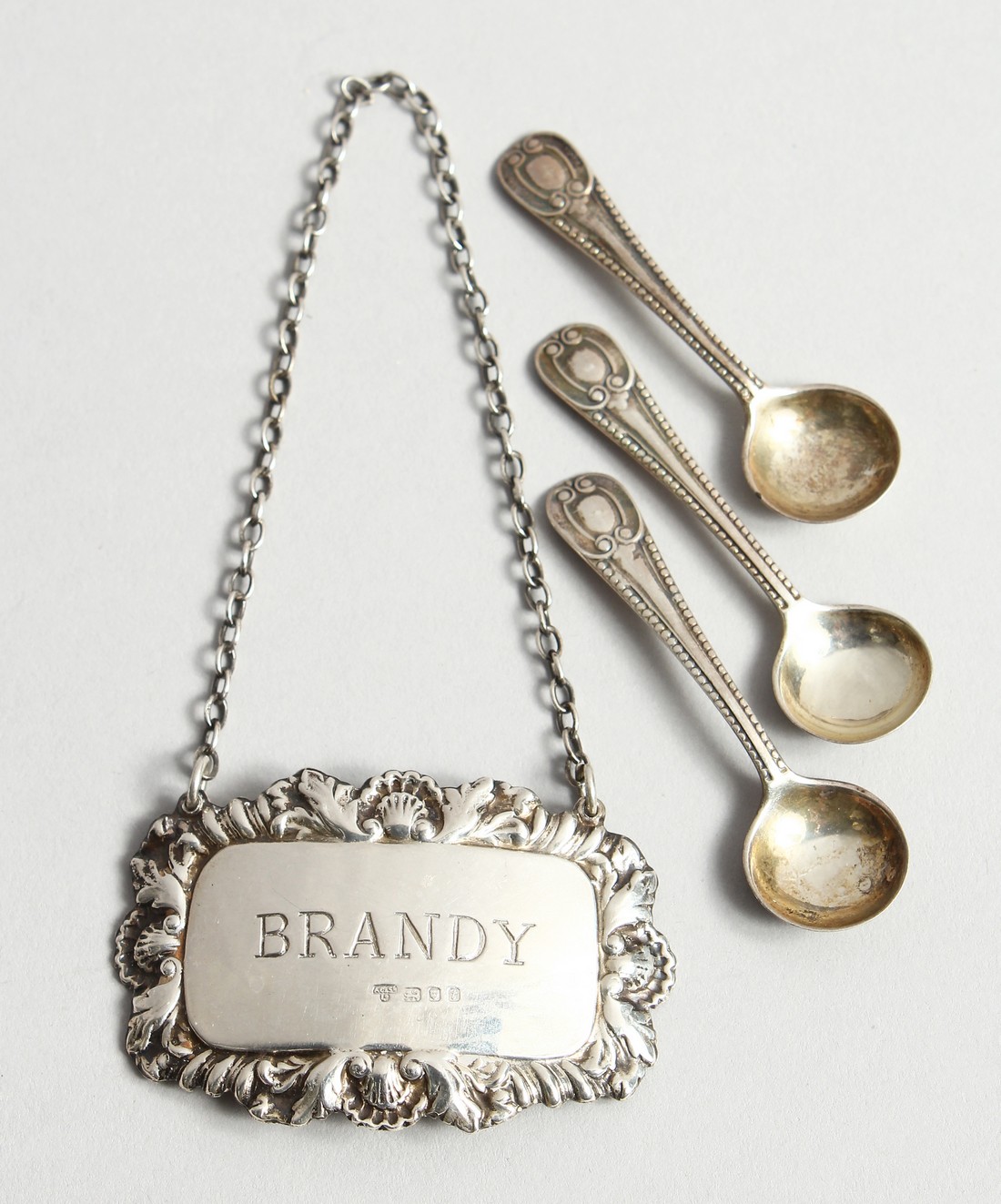 A SILVER BRANDY LABEL AND THREE SALT SPOONS