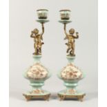 A PAIR OF CONTINENTAL PORCELAIN CUPID CANDLESTICKS on gilt bases. 14ins high.