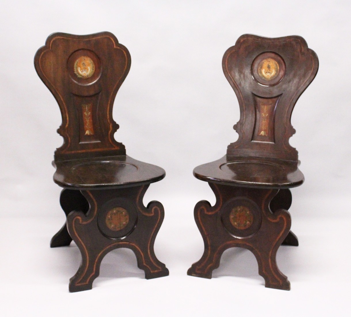 A GOOD PAIR OF REGENCY MAHOGANY HALL CHAIRS with shaped backs with painted crest, solid seats