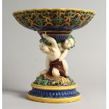 A MINTON MAJOLICA COMPORT, modelled as a pair of cherubs holding aloft a bowl. (AF) 9ins high