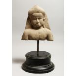A CAMBODIAN CARVED STONE FRAGMENTARY BUST, mounted on a circular base 18ins high.