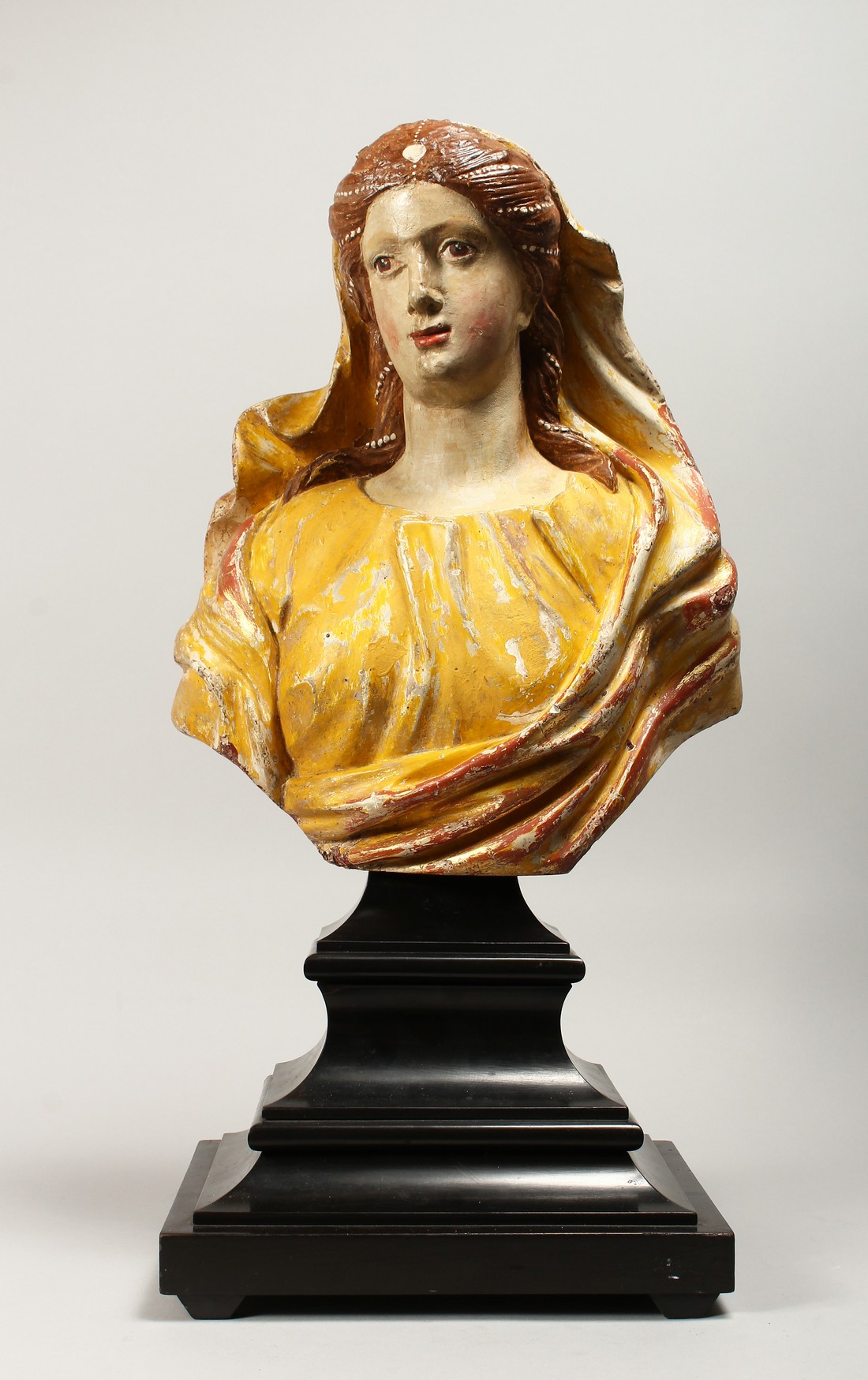 A 18TH CENTURY WOOD AND POLYCHROME DECORATED BUST OF A YOUNG LADY, on ebonised stepped base Bust