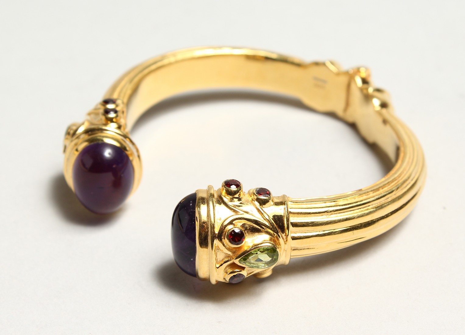 A GOOD TORQUE STYLE SPRING GILDED SILVER BANGLE, set with a pair of cabochon amethysts, two pear