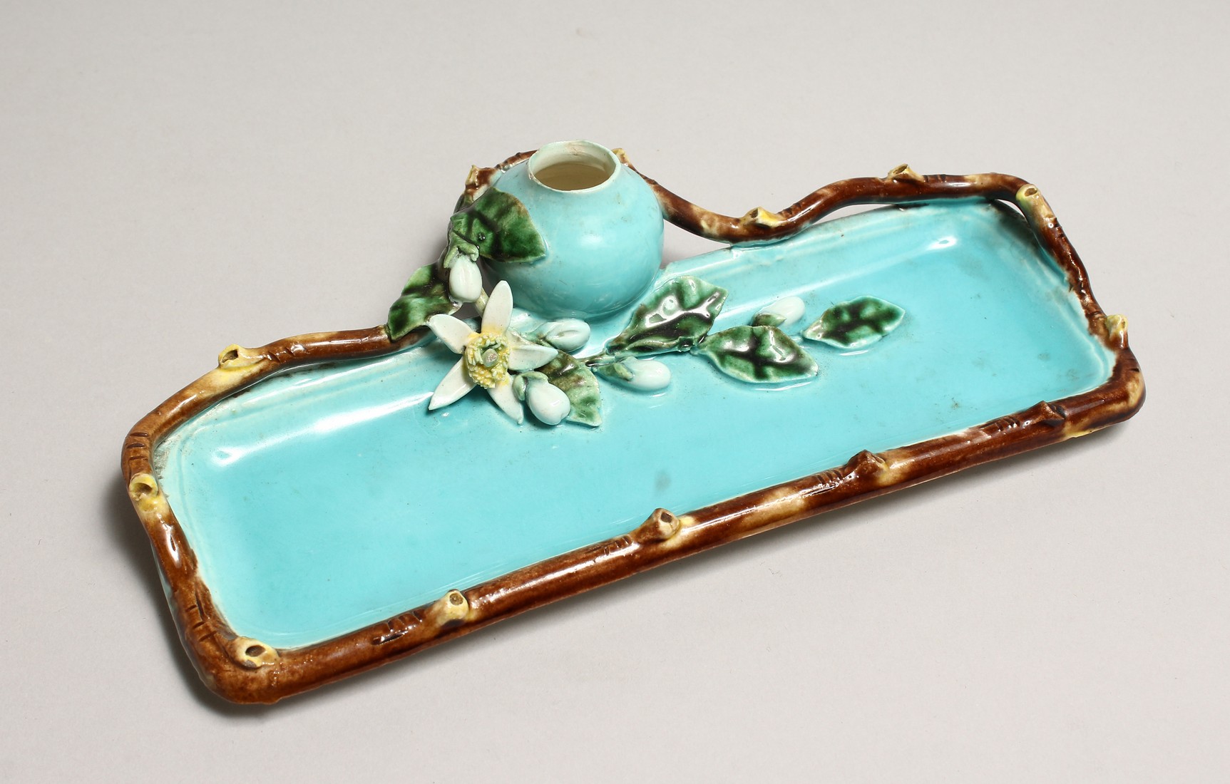 A MAJOLICA TURQUOISE GLAZED DESK STAND with inkwell, of naturalistic form. 9ins long.