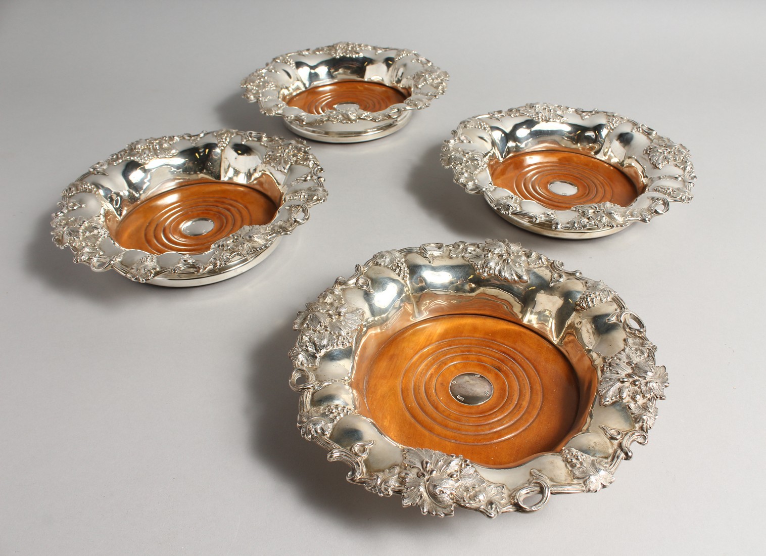 A VERY GOOD SET OF FOUR VICTORIAN SILVER WINE COASTERS with fruiting vine decoration and turned wood