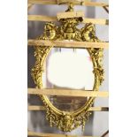 A LARGE IMPRESSIVE GILT FRAMED OVAL MIRROR, the frame mounted with a cherub seated on an urn, with