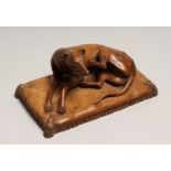 AFTER GOTT. A CARVED WOOD FIGURE OF A DOG on a cushion 6ins long