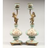 A PAIR OF ORNATE PORCELAIN AND ORMOLU CANDLESTICKS with cherub supports. 14ins high.